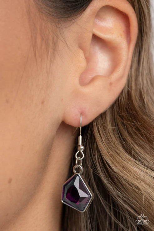 Close-up of an ear wearing a purple teardrop earring with a silver hook.