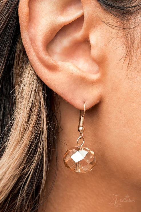 Close-up of a person wearing a gold earring with a clear gemstone.