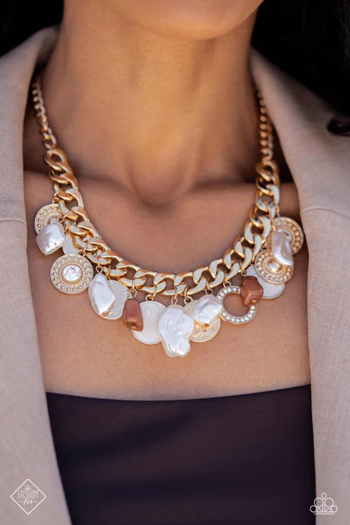 Gold chain necklace with various pendants on a person wearing a beige jacket.