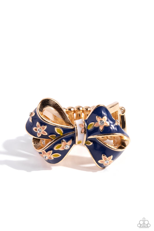 Gold and blue bow-shaped ring with floral details on a white background