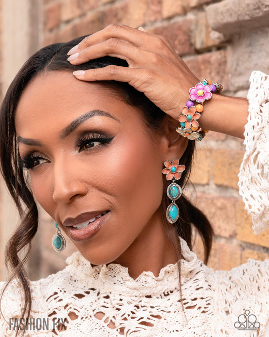 Woman wearing colorful floral earrings and bracelet against a brick wall.