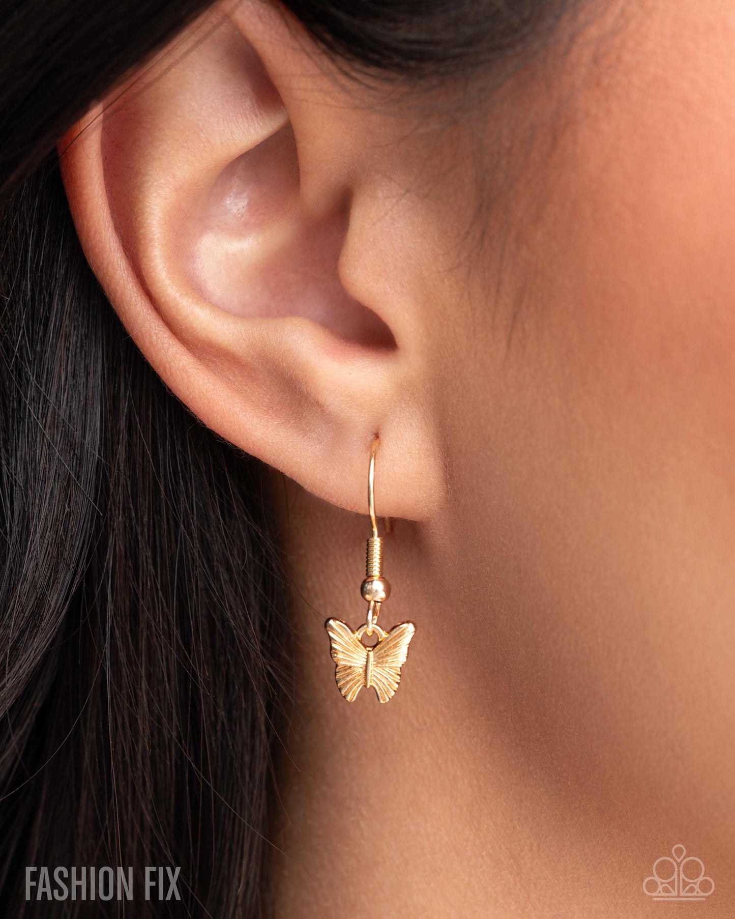 Gold butterfly earring worn by a person with dark hair.