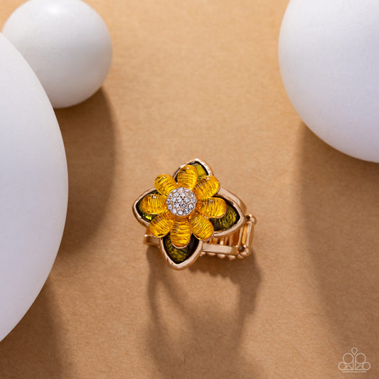 Gold flower-shaped earring with yellow and green accents on a beige background