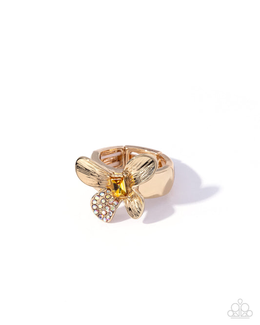 A gold-tone butterfly ring with a central yellow gemstone and a heart-shaped cluster of small clear crystals, photographed on a white background with a soft shadow.