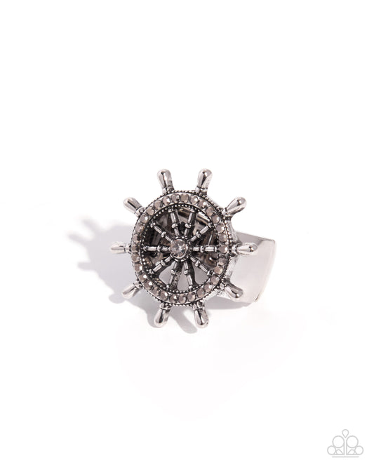 Silver steering wheel-shaped ring with black center on a white background