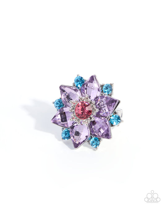 A floral-shaped ring featuring lavender purple crystals, a central pink crystal, and small light blue crystals on a white background.