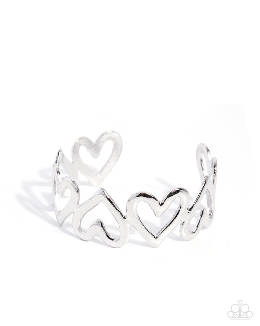 A silver open cuff ring featuring a continuous pattern of interlocking hearts, photographed on a clean white background with a soft shadow.