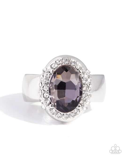 A silver-toned halo ring featuring a large oval faceted dark plum-purple center stone surrounded by a halo of small clear stones, shown on a white background.