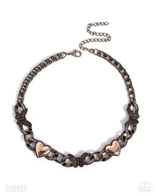 An antique bronze chain necklace with butterfly and heart charms, displayed on a clean white background.