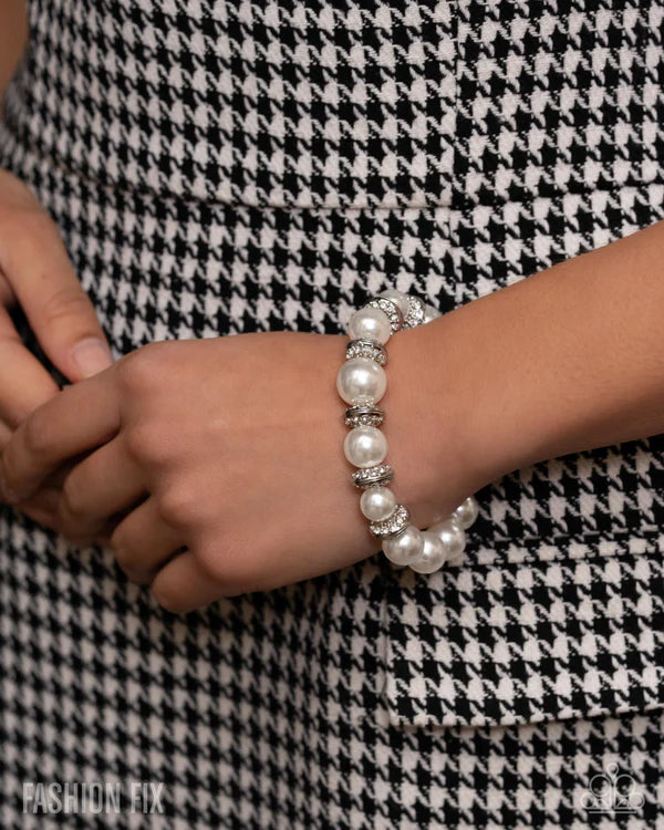 Pearl bracelet on a wrist against a black and white checkered background