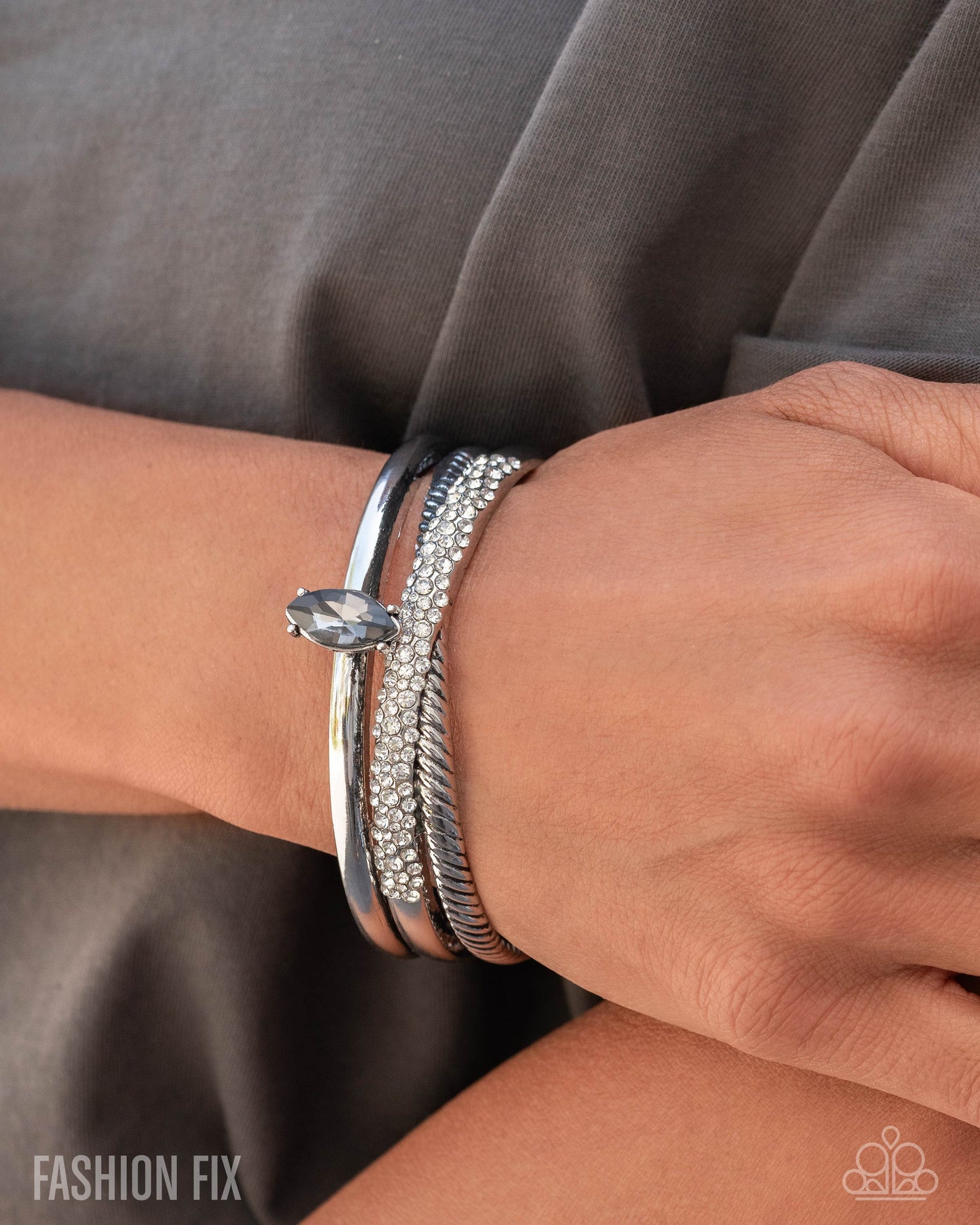 Close-up of a wrist wearing multiple silver bracelets with a gray background