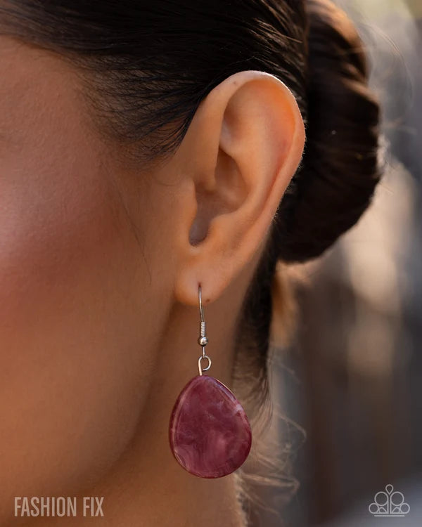 Close-up of an ear wearing a pink earring with blurred background
