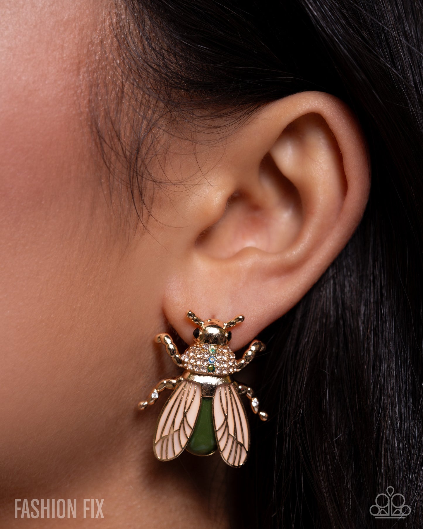 Close-up of an ear wearing a gold bee-shaped earring with green gemstone.