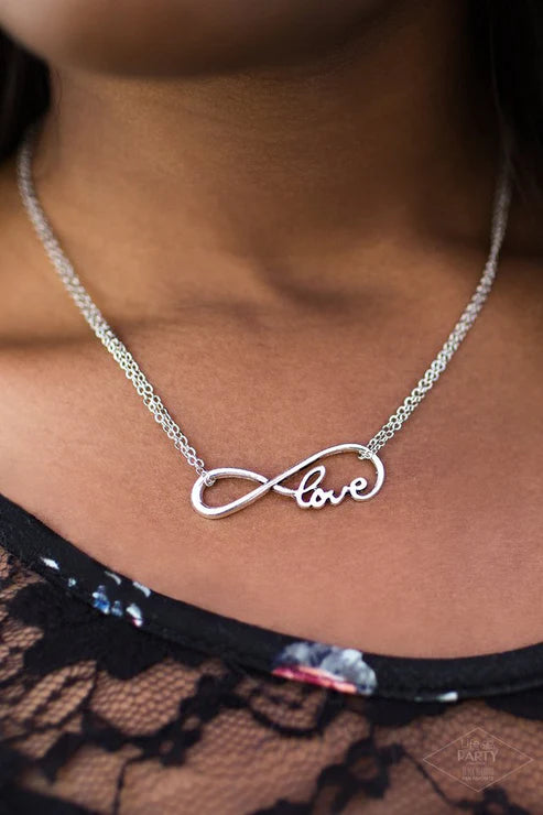 Silver necklace with infinity and 'love' pendant on a person wearing a black lace garment.