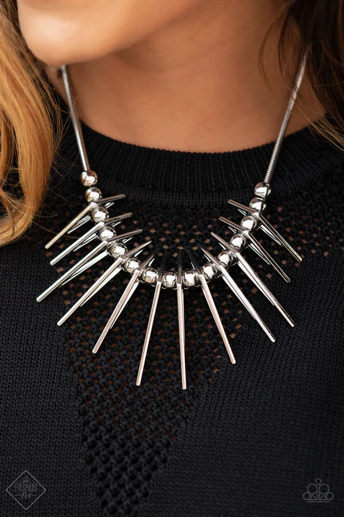 Silver spike necklace worn by a person against a black background
