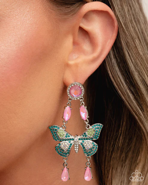 Butterfly-shaped earring with pink and green accents worn by a person.