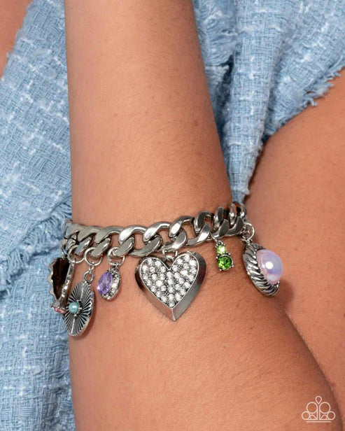 Silver chain bracelet with heart and other charms on a wrist against a denim background