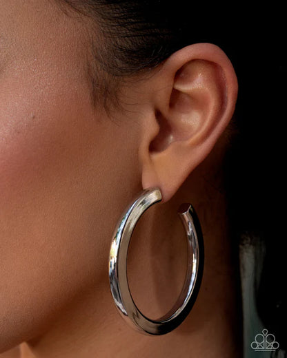 Silver hoop earring worn on an ear with a dark background