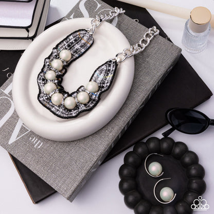 Pearl necklace on a white plate with sunglasses and black beads in the background