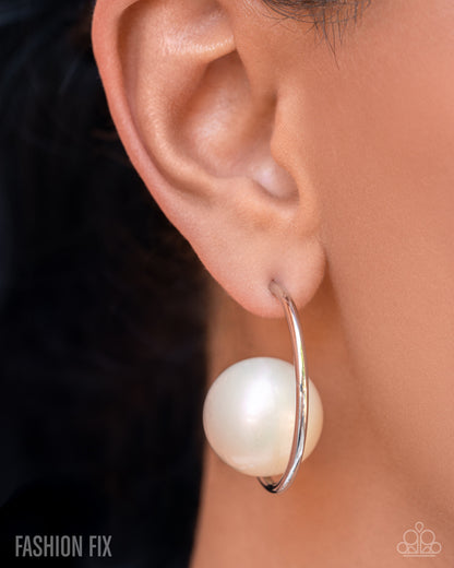 Close-up of an ear wearing a silver hoop earring with a large white bead.