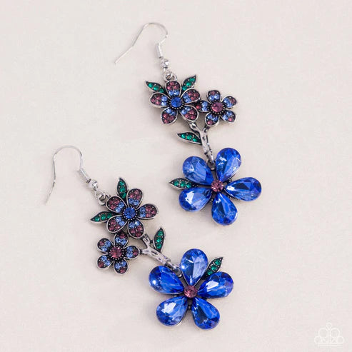 Pair of floral earrings with blue and purple gemstones on a light background