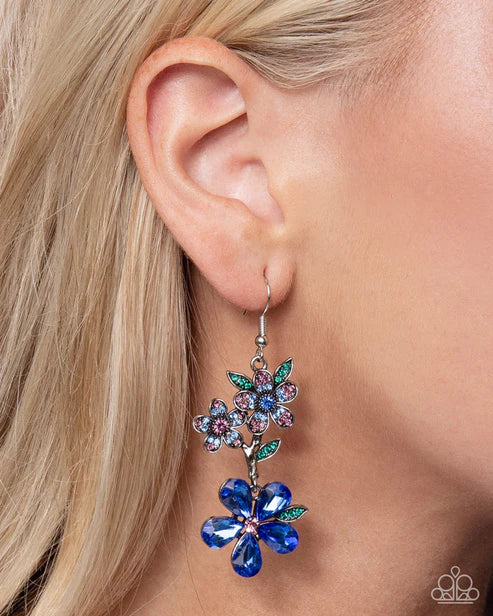 Close-up of an ear wearing a colorful floral earring with blue gemstones.