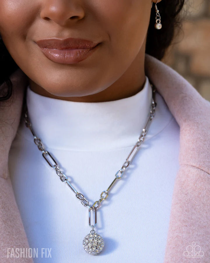 Close-up of a woman wearing a silver necklace with a pendant, against a neutral background.