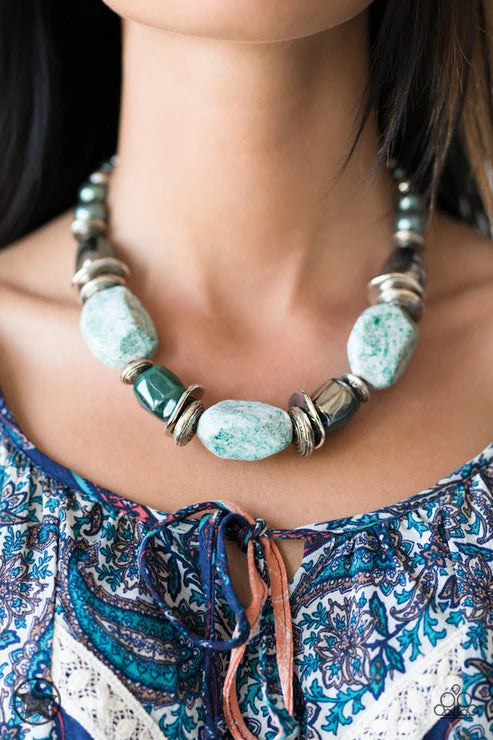 Necklace with large turquoise beads worn by a person in a patterned top.