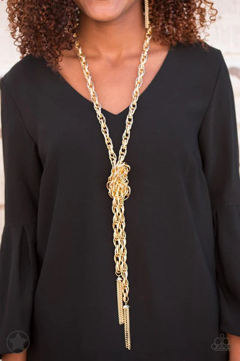 Person wearing a long gold chain necklace on a plain background
