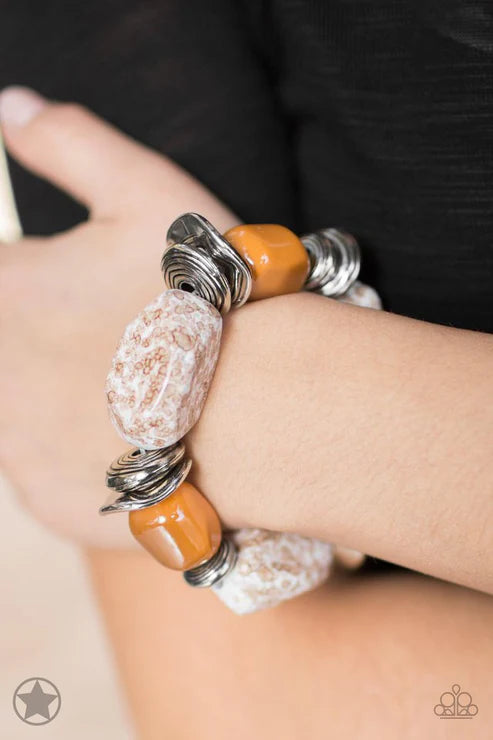 Close-up of a hand wearing a bracelet with orange, silver, and white beads on a dark background
