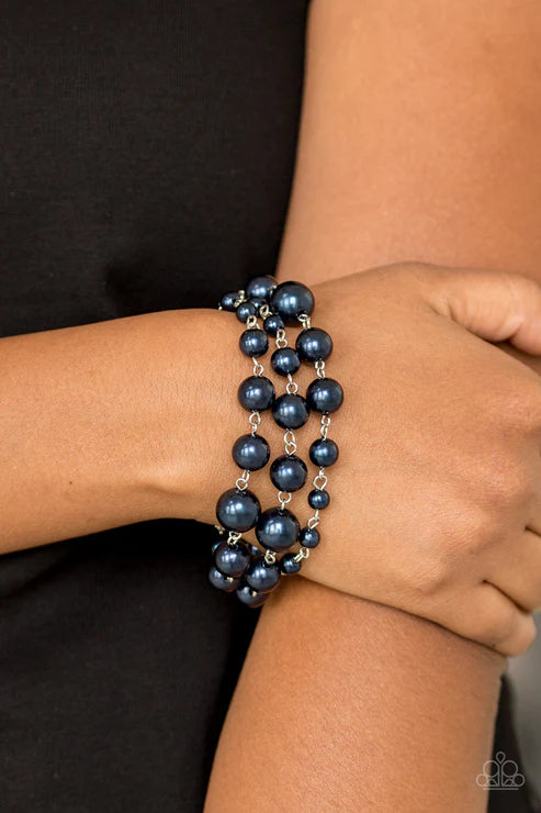 Close-up of a wrist wearing two blue pearl bracelets against a black background