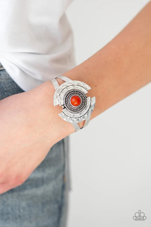 Silver bracelet with a red stone on a wrist against a white background