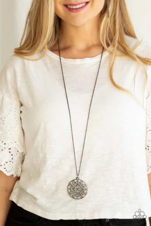 Woman wearing a long necklace with a decorative pendant on a plain background