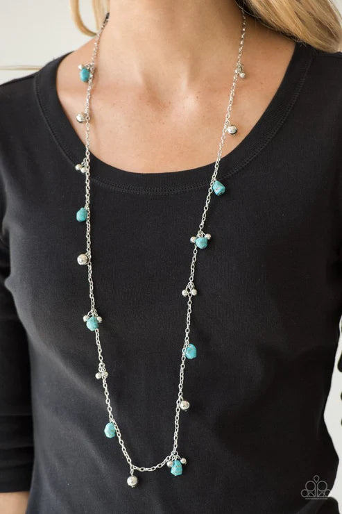 Necklace with turquoise beads and silver chain worn by a person on a black shirt