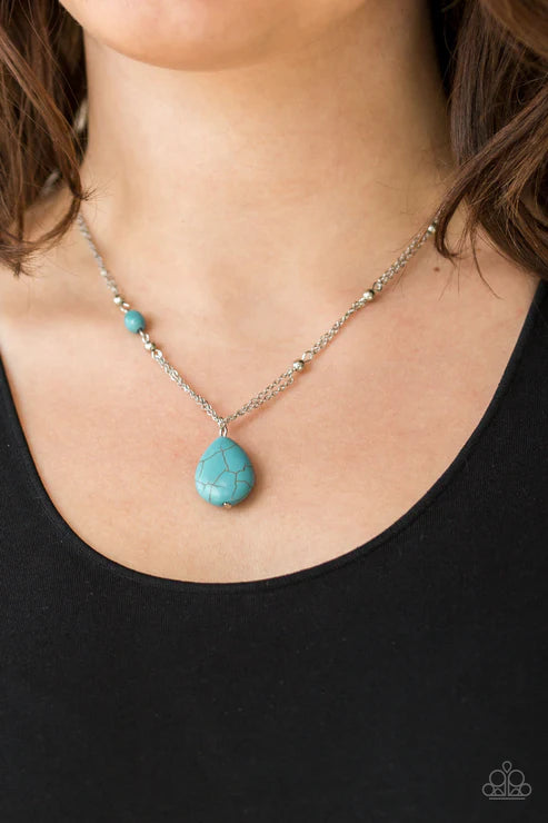 Turquoise necklace with a teardrop pendant on a person wearing a black top.