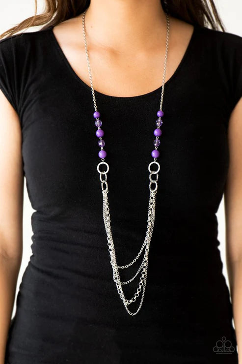 Long silver chain necklace with purple beads on a black shirt