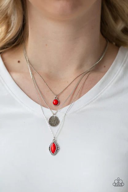 Person wearing two silver necklaces with red pendants on a white background