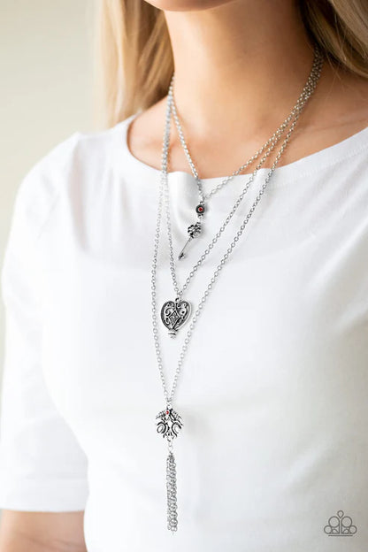Layered silver necklaces with heart and tassel pendants on a white shirt.
