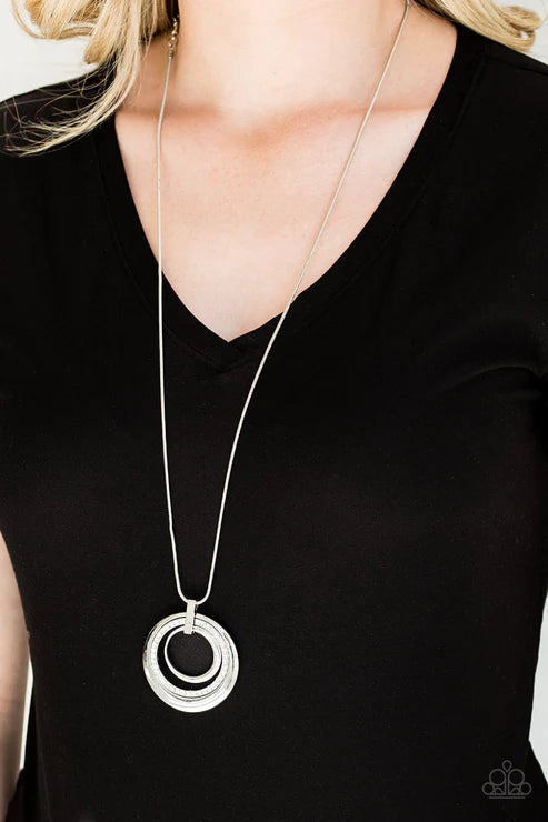 Person wearing a black top with a long silver necklace featuring two interlocking rings.