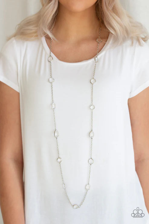 Long necklace worn by a person in a white top against a neutral background