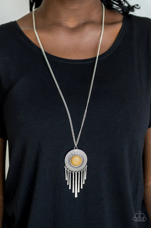 Person wearing a long necklace with a pendant on a plain background