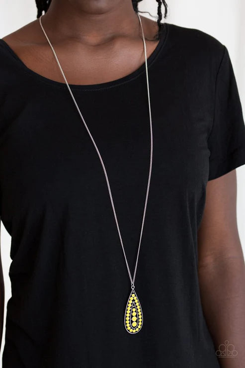 Person wearing a black shirt with a long necklace featuring a yellow teardrop pendant.