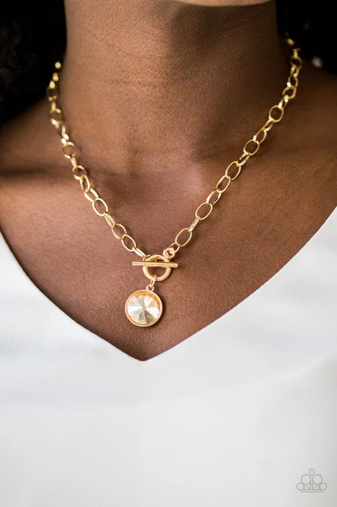 Gold necklace with a round pendant on a person wearing a white shirt