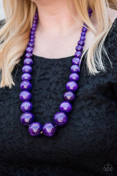 Purple beaded necklace worn by a person with blonde hair against a black lace background