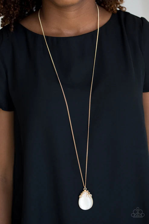 Person wearing a gold necklace with a white pendant on a black background