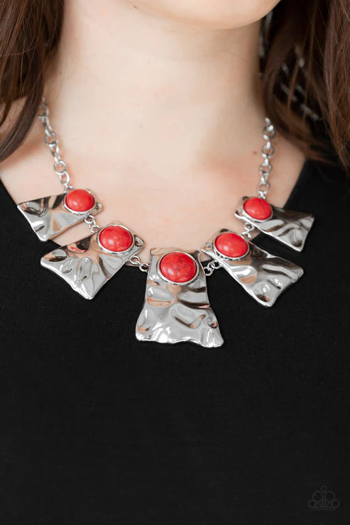 Silver necklace with red stones worn by a person against a black background