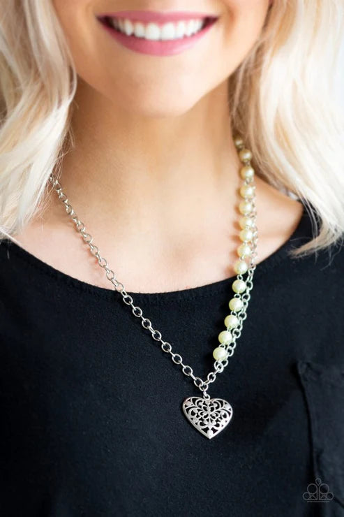Necklace with heart pendant worn by a person with blonde hair and a black top.