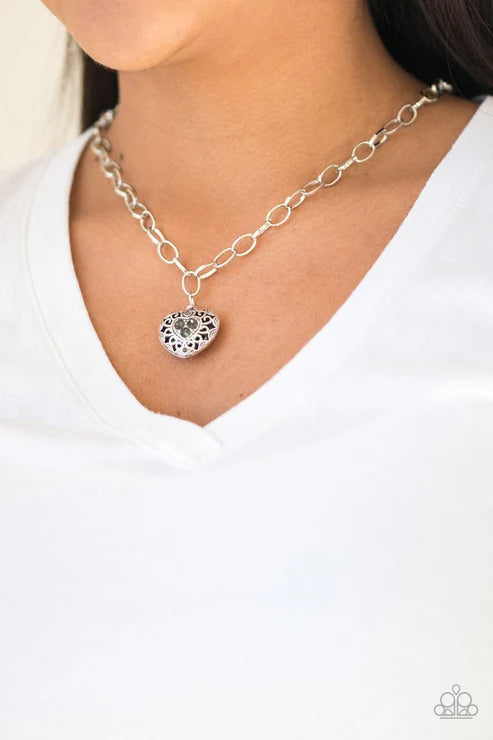 Silver chain necklace with a heart pendant worn by a person in a white shirt.