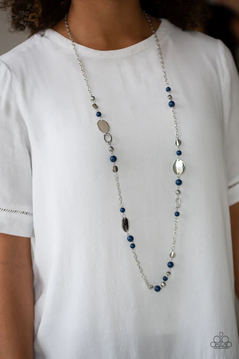 Person wearing a long beaded necklace with blue and silver beads on a plain background