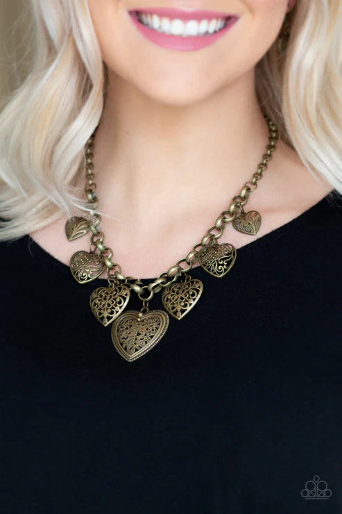 Gold heart-shaped necklace worn by a person with blonde hair against a black background